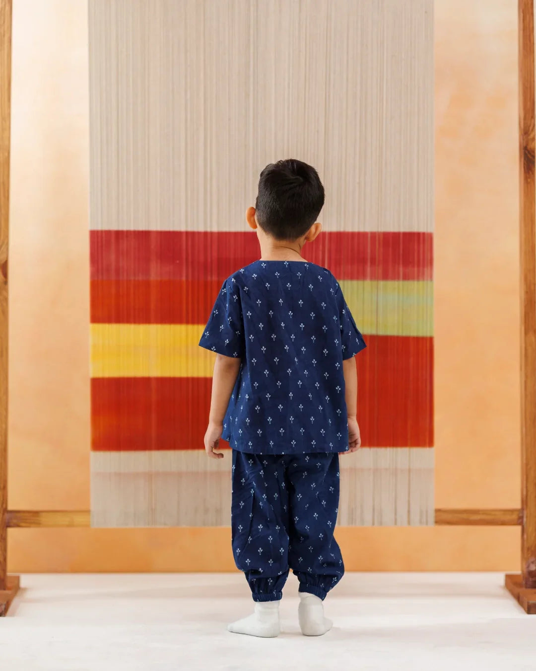 Toddler in blue organic cotton block print kurta pajama set standing by colorful loom