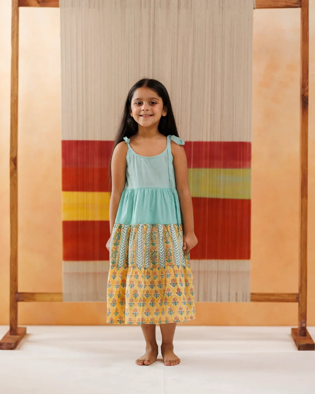 Young girl wearing sleeveless tiered cotton dress with floral and block print patterns