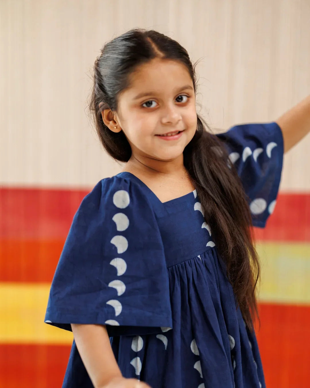 Smiling girl in navy organic cotton dress with moon phase block print, kidswear fashion