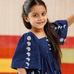 Smiling girl in navy organic cotton dress with moon phase block print, kidswear fashion