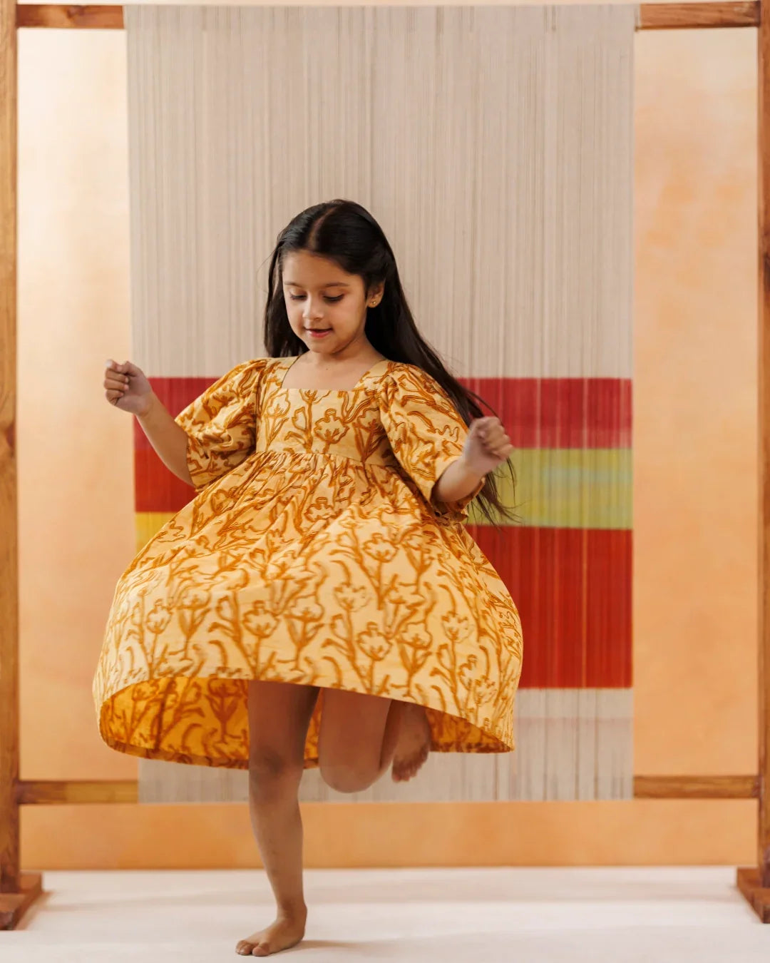 Young girl in yellow organic cotton block print dress, twirling indoors, kids fashion
