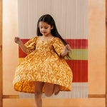 Young girl in yellow organic cotton block print dress, twirling indoors, kids fashion
