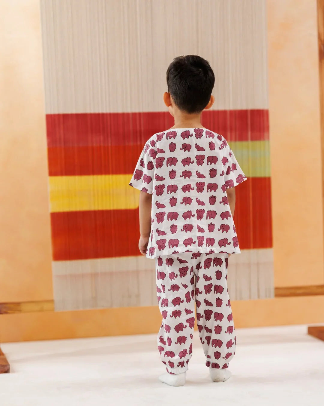 Toddler wearing white organic cotton pajama set with pink elephant print, standing indoors