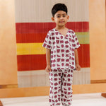 Young boy wearing organic cotton elephant print pajamas, standing indoors against a colorful textile backdrop