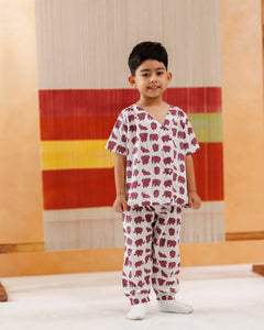 Young boy wearing organic cotton elephant print pajamas, standing indoors against a colorful textile backdrop