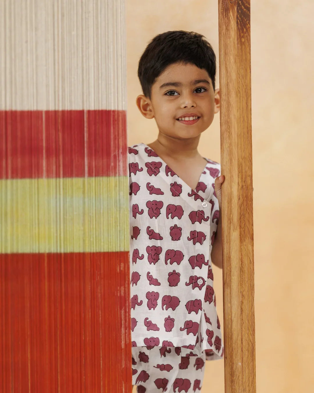 Child in organic cotton pajamas with pink elephant print, smiling indoors