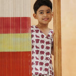 Smiling child in organic cotton elephant print kidswear peeking from behind a colorful textile panel