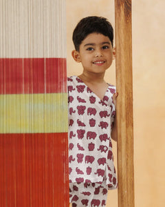 Smiling child in organic cotton elephant print kidswear peeking from behind a colorful textile panel
