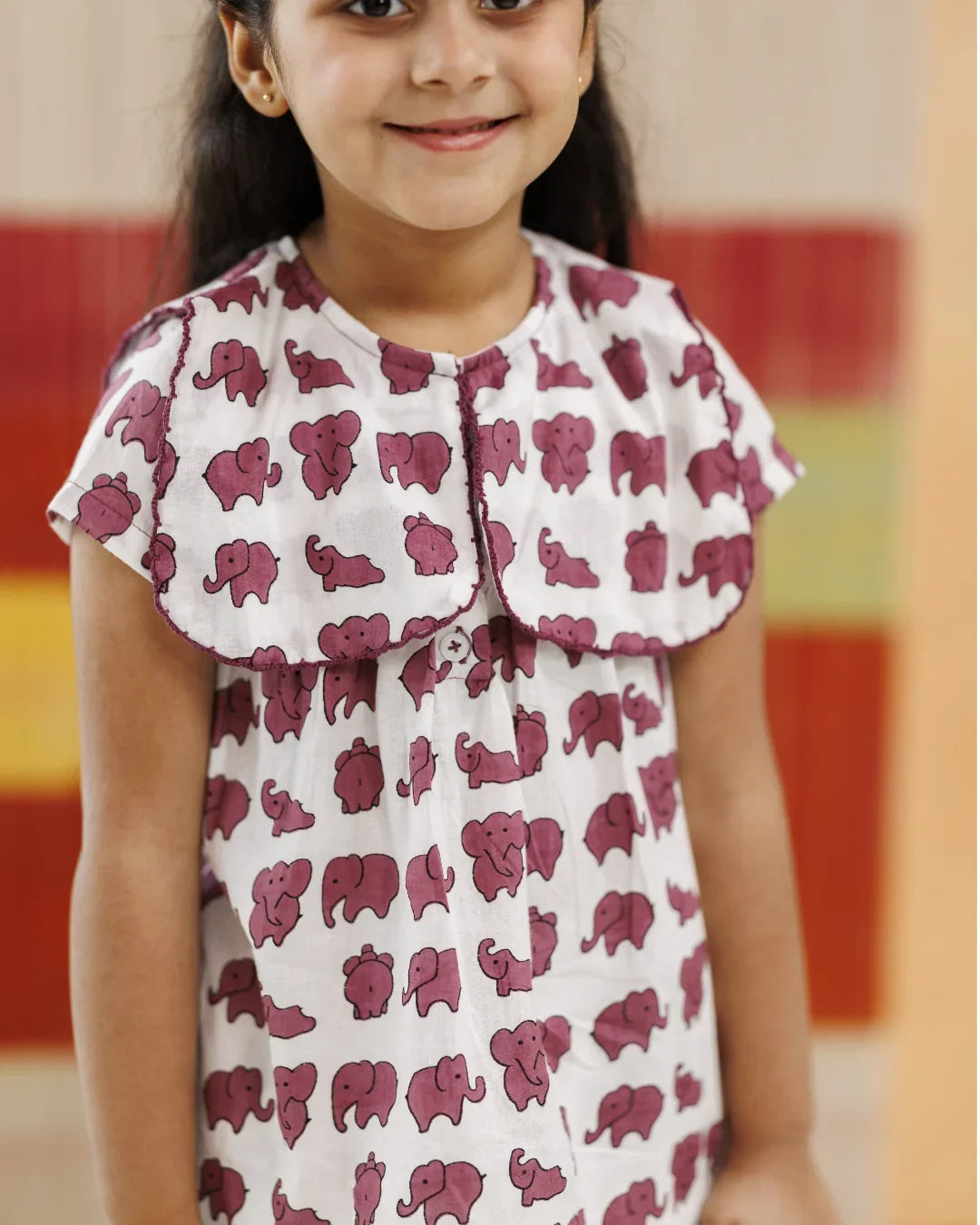 Girl wearing white organic cotton dress with purple elephant block print, smiling indoors