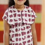 Girl wearing white organic cotton dress with purple elephant block print, smiling indoors