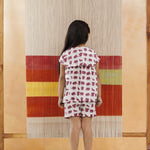 Young child in organic cotton elephant print shorts set, standing indoors by a woven textile backdrop.