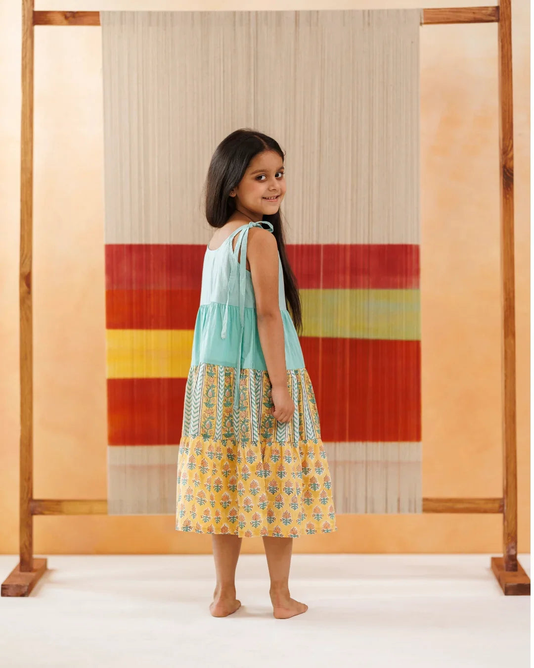 Young girl in a sleeveless block print cotton dress with floral patterns, standing indoors