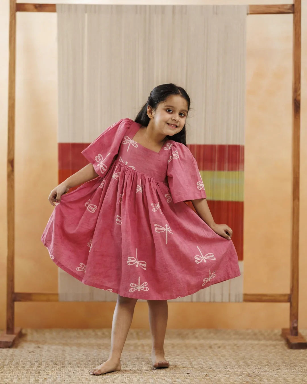 Smiling girl in pink organic cotton dress with white dragonfly print, playful kidswear fashion