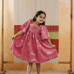 Smiling girl in pink organic cotton dress with white dragonfly print, playful kidswear fashion