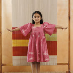 Young girl in a pink organic cotton dress with white dragonfly prints, standing arms outstretched