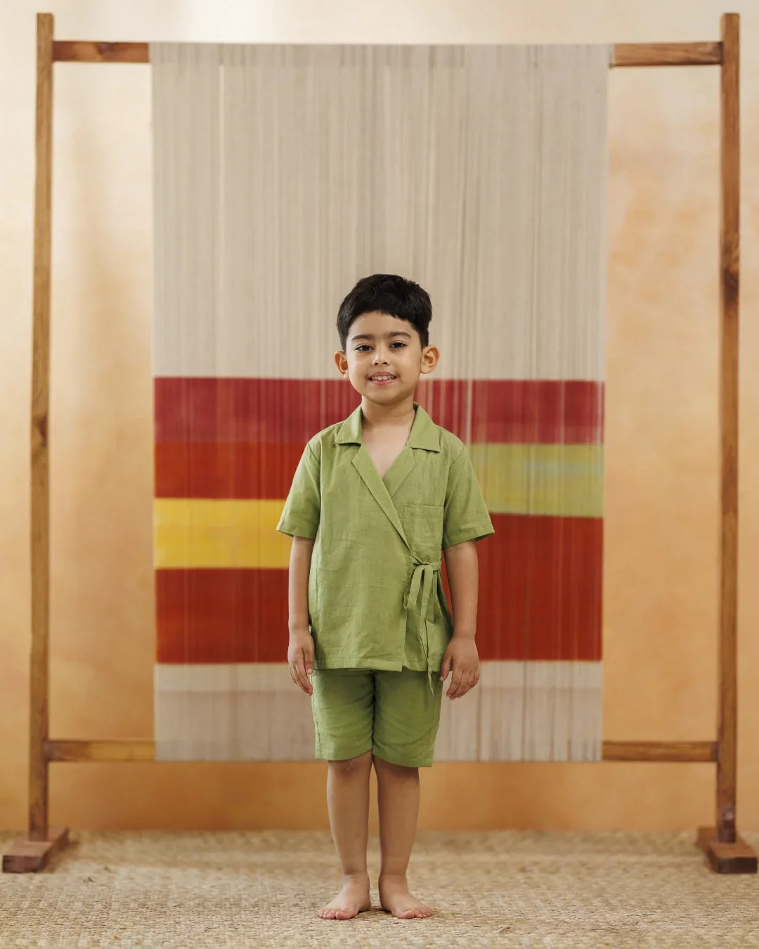 Smiling boy in green organic cotton kidswear shorts and shirt, standing indoors