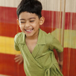 Smiling child in light green wrap shirt, standing indoors against a colorful striped backdrop