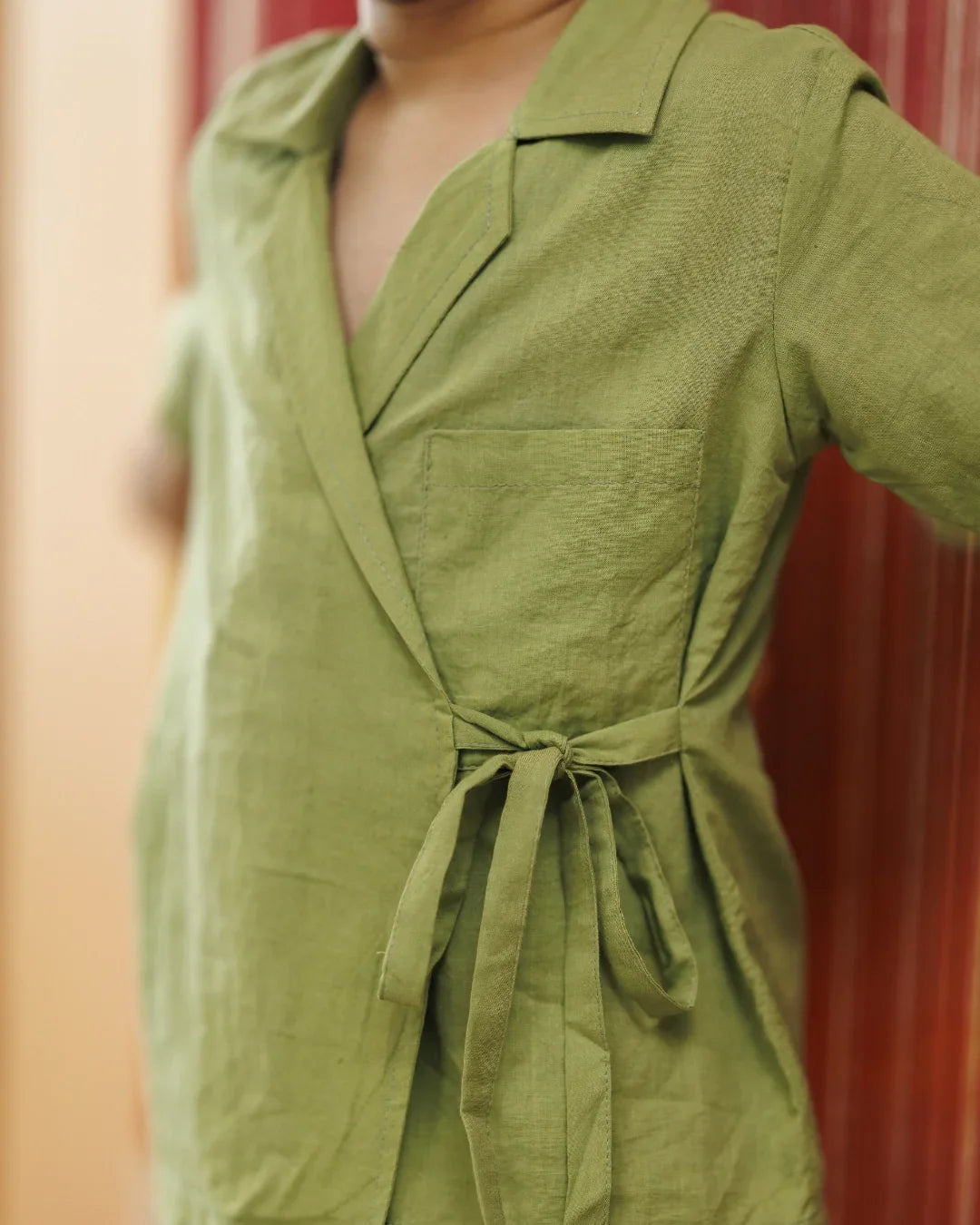 Child wearing green organic cotton wrap dress with tie detail and front pocket