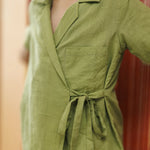 Child wearing green organic cotton wrap dress with tie detail and front pocket