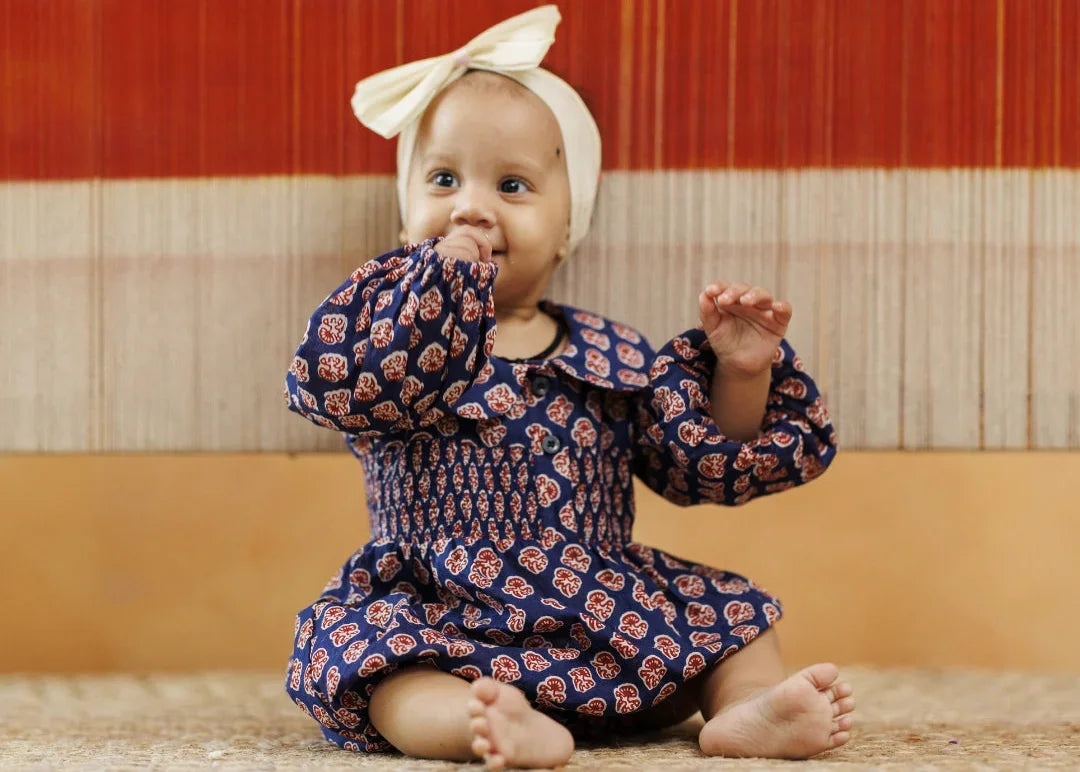 Baby wearing navy blue organic cotton block print dress and cream headband, sitting indoors
