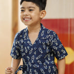 Smiling young boy in blue organic cotton wrap shirt with white fish print, indoor setting