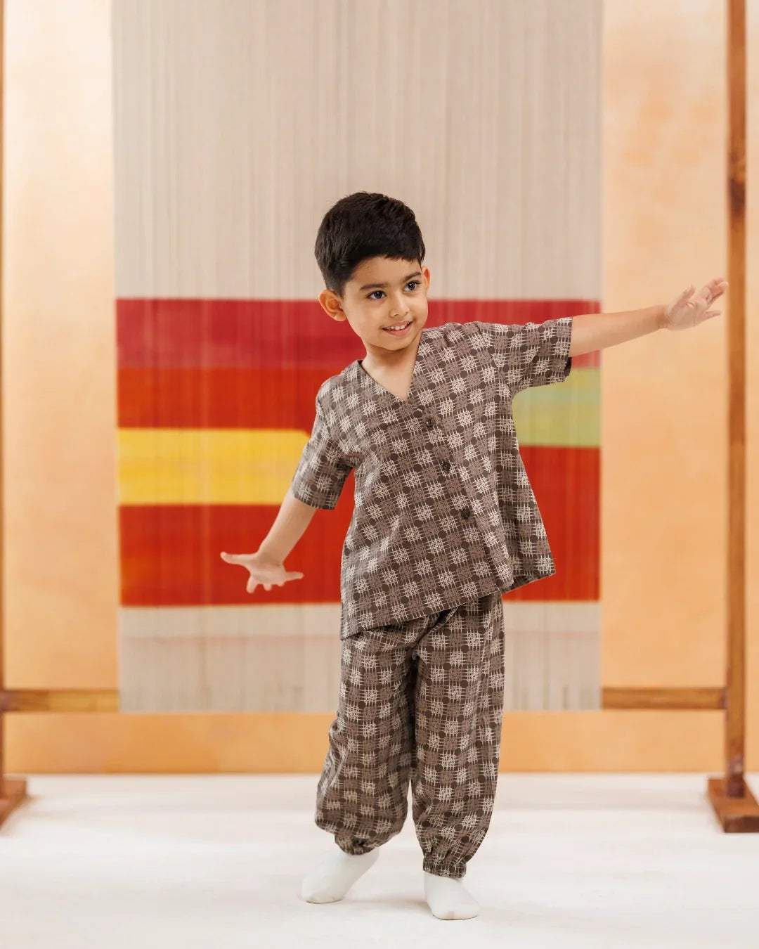 Young boy in organic cotton block print kidswear set, standing indoors with colorful textile backdrop.