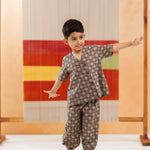 Young boy in organic cotton block print kidswear set, standing indoors with colorful textile backdrop.
