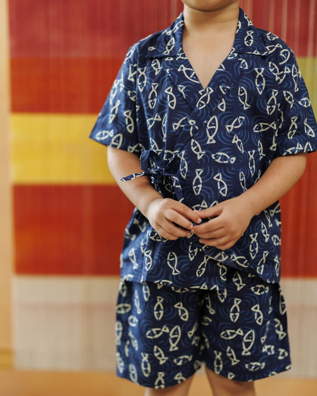 Child wearing navy blue organic cotton shorts set with cream fish print, standing indoors
