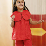 Smiling young girl wearing red organic cotton top and shorts set with scalloped collar indoors