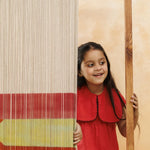 Smiling young girl in a red cotton dress peeking from behind a colorful textile panel
