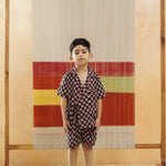 Young boy in organic cotton printed black kimono set stands indoors against a woven textile backdrop.
