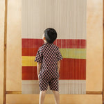 Young boy in organic cotton block print shirt and shorts, facing a colorful woven textile