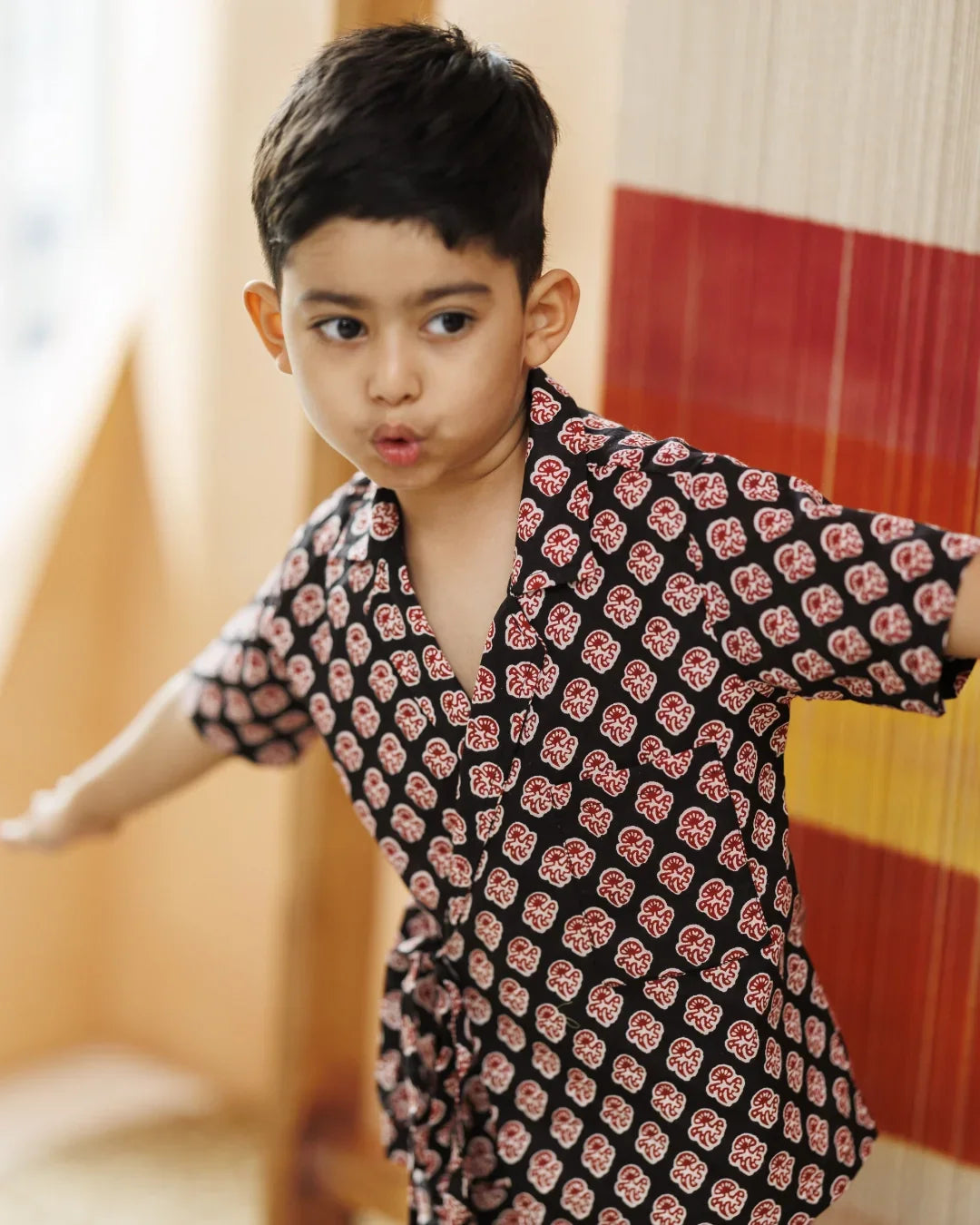 Young boy wearing black organic cotton shirt with red block print pattern, playful indoors
