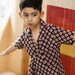 Young boy wearing black organic cotton shirt with red block print pattern, playful indoors