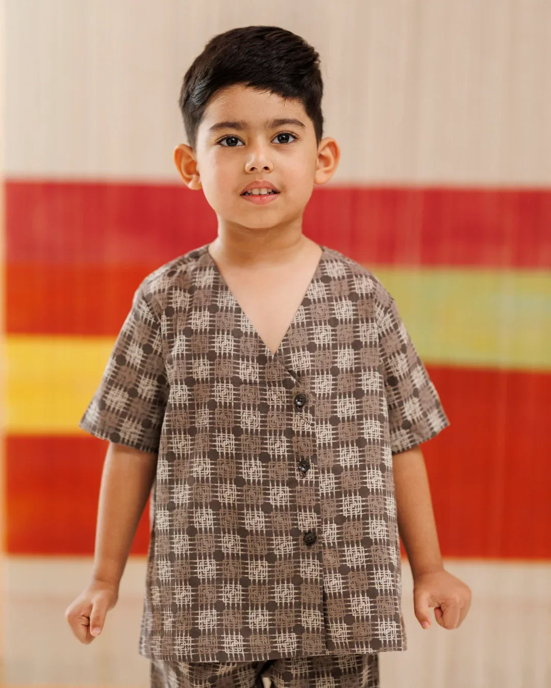 Young boy in brown checkered organic cotton shirt and shorts, standing indoors.