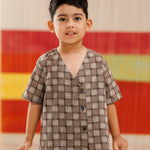 Young boy in brown checkered organic cotton shirt and shorts, standing indoors.