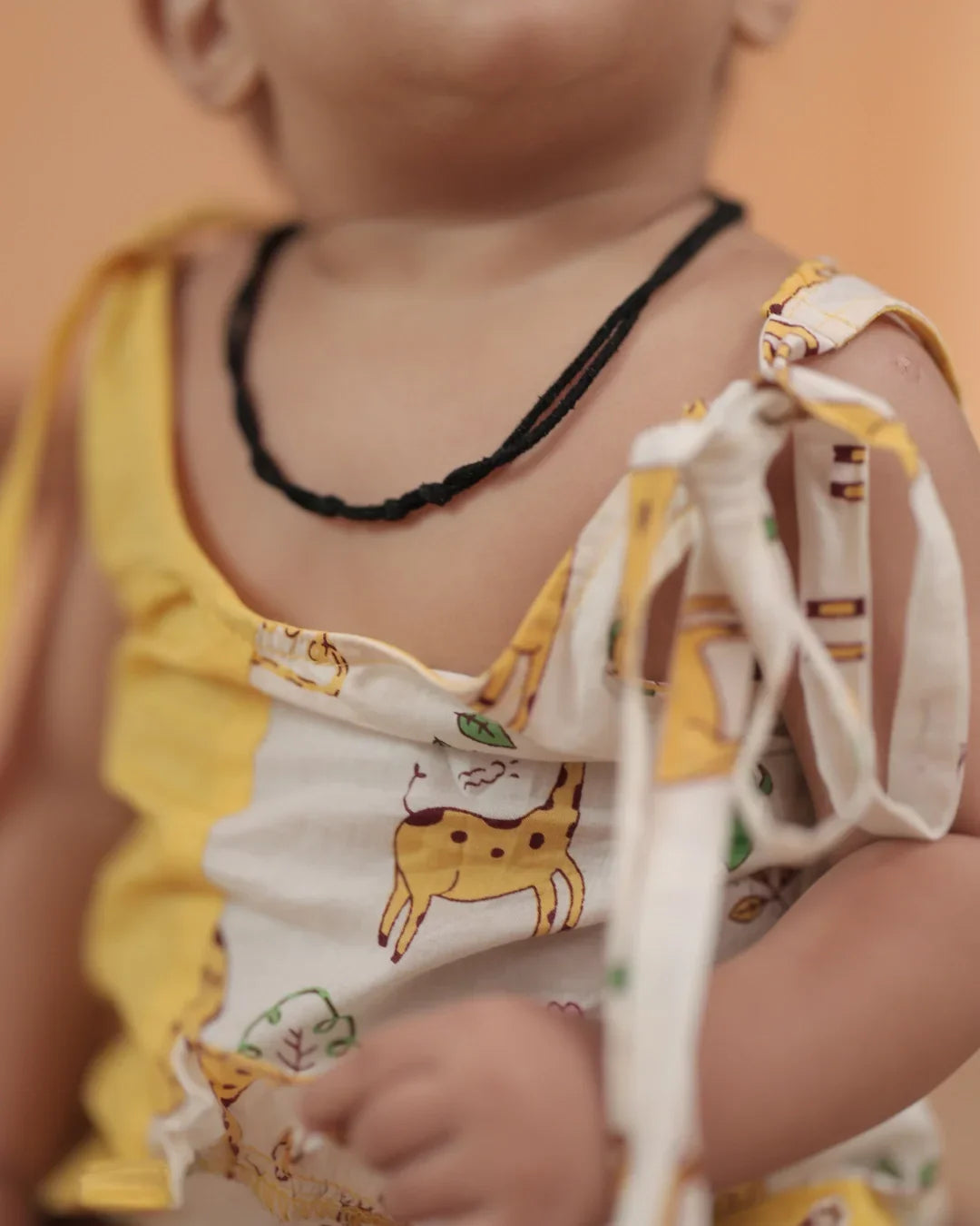 Baby wearing organic cotton sleeveless romper with yellow animal print and shoulder tie.