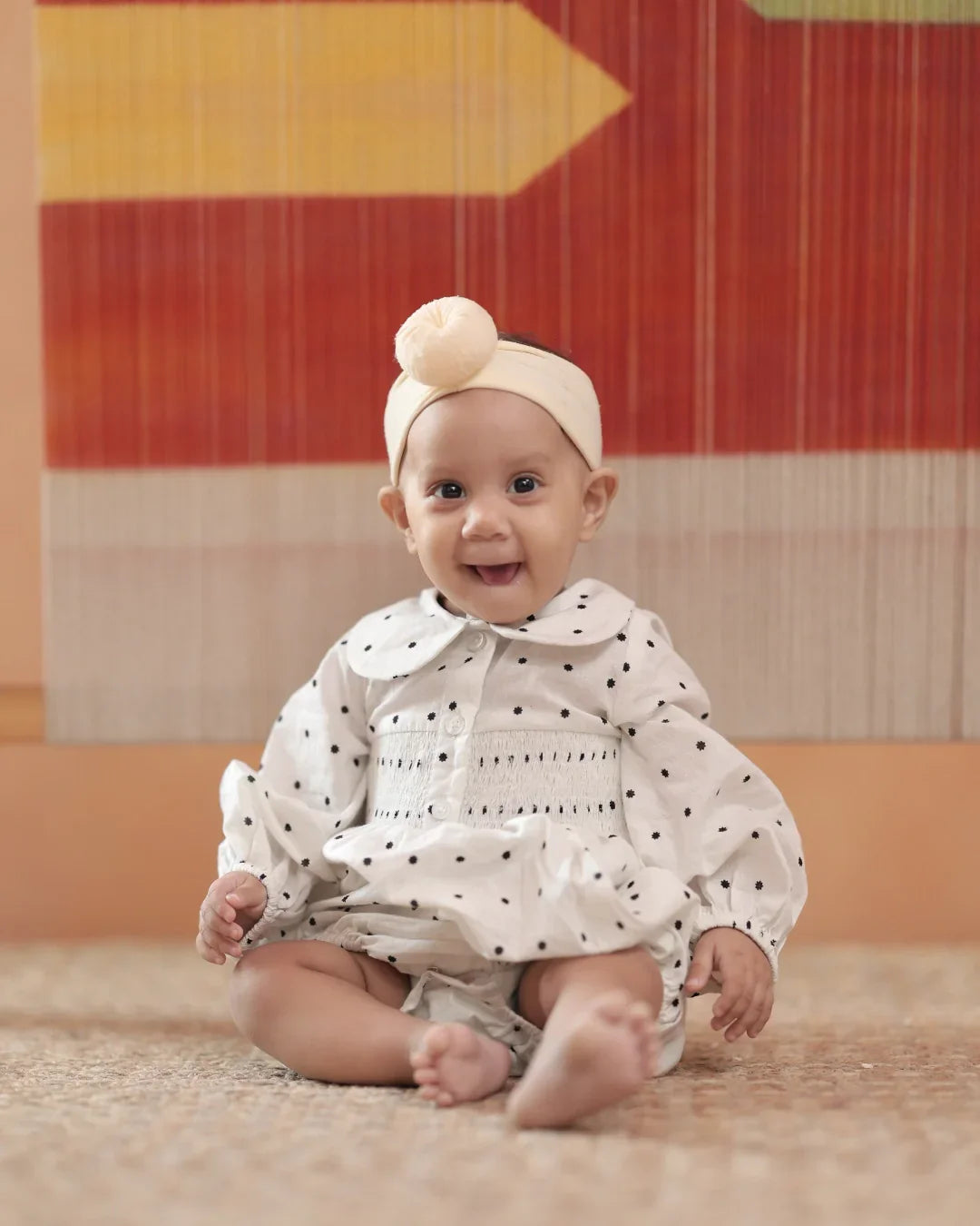 Smiling baby wearing organic cotton polka dot dress and headband, sitting indoors