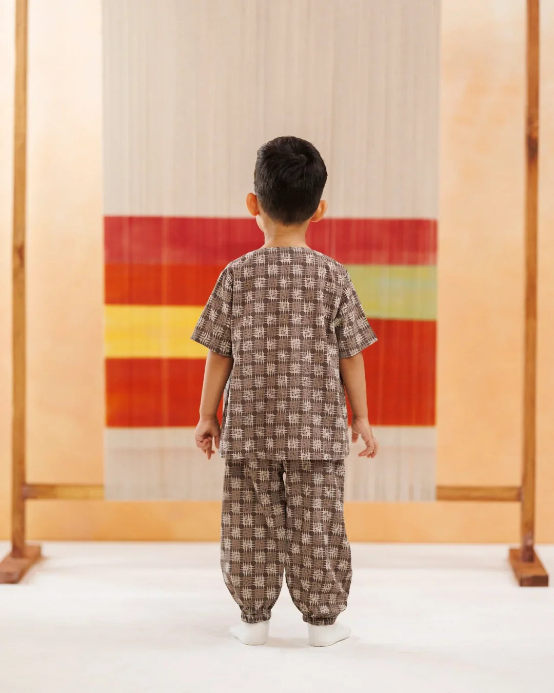 Toddler wearing brown block print organic cotton top and pants, standing indoors.