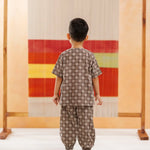 Young child wearing brown cotton block print co-ord set, facing abstract colorful textile backdrop.