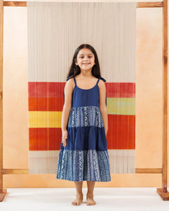 Young girl in a blue organic cotton sundress with white block print pattern, standing barefoot