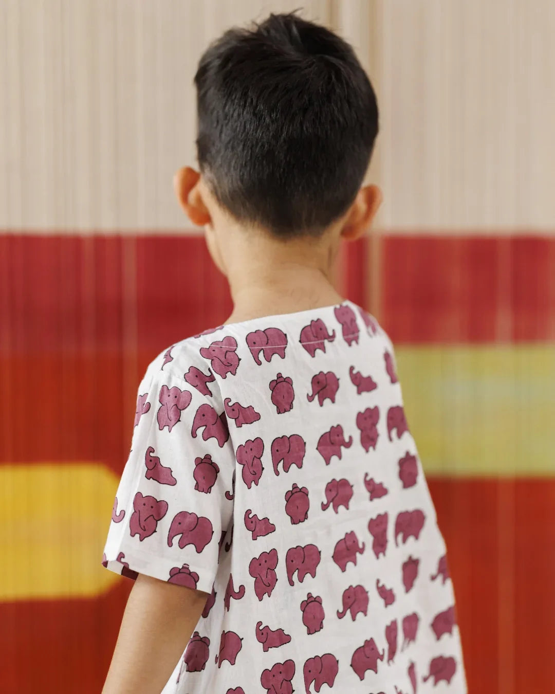 Toddler in white organic cotton t-shirt with pink elephant print, colorful background