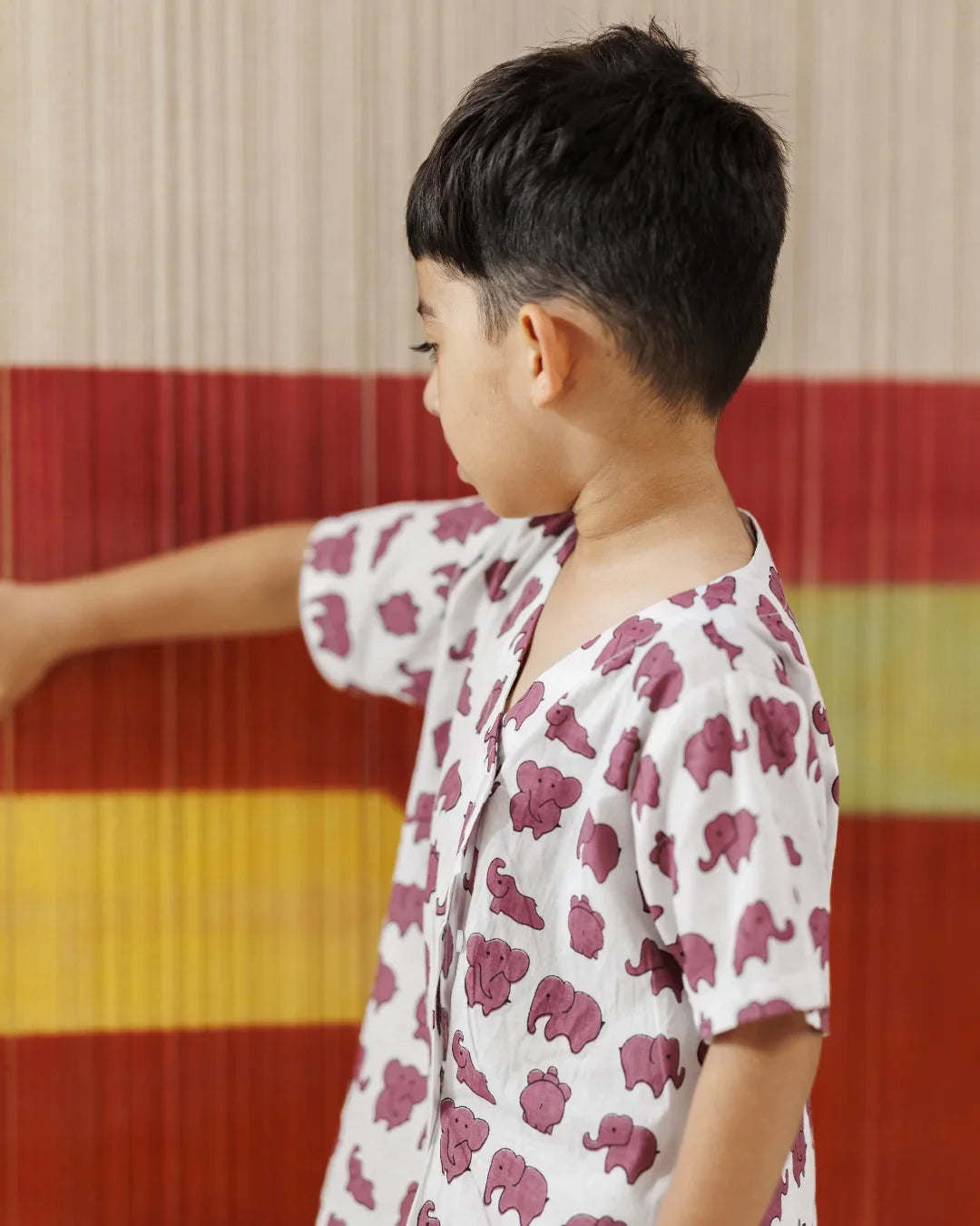 Young child in white shirt with purple elephant print, standing against striped background