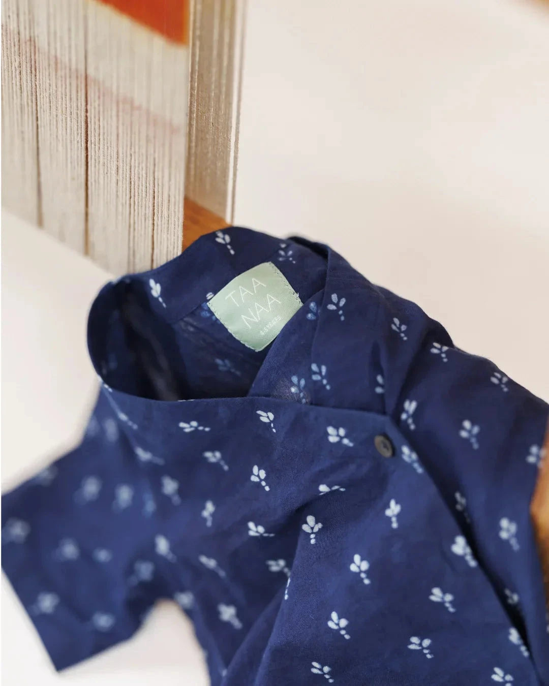 Navy blue organic cotton kids shirt with white block print floral pattern hanging by loom.