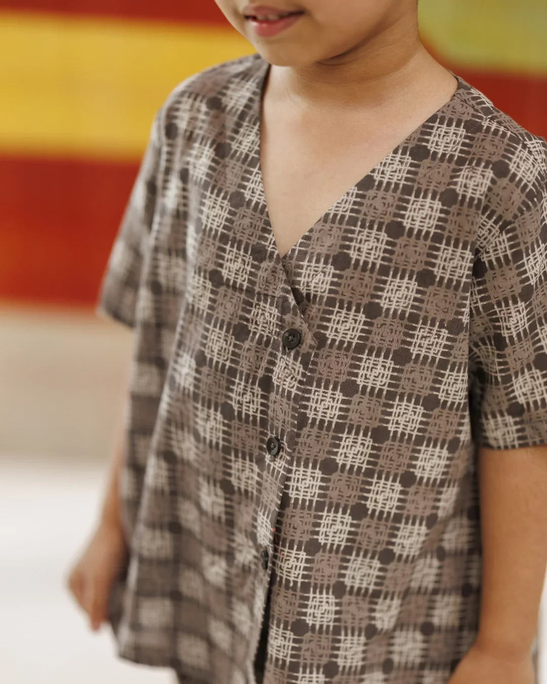 Child wearing a brown organic cotton shirt with abstract block print and v-neck design