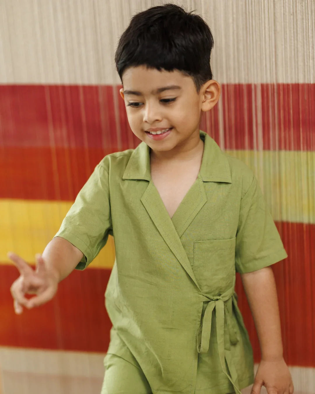 Smiling boy in green organic cotton wrap top and shorts, kidswear, playing indoors