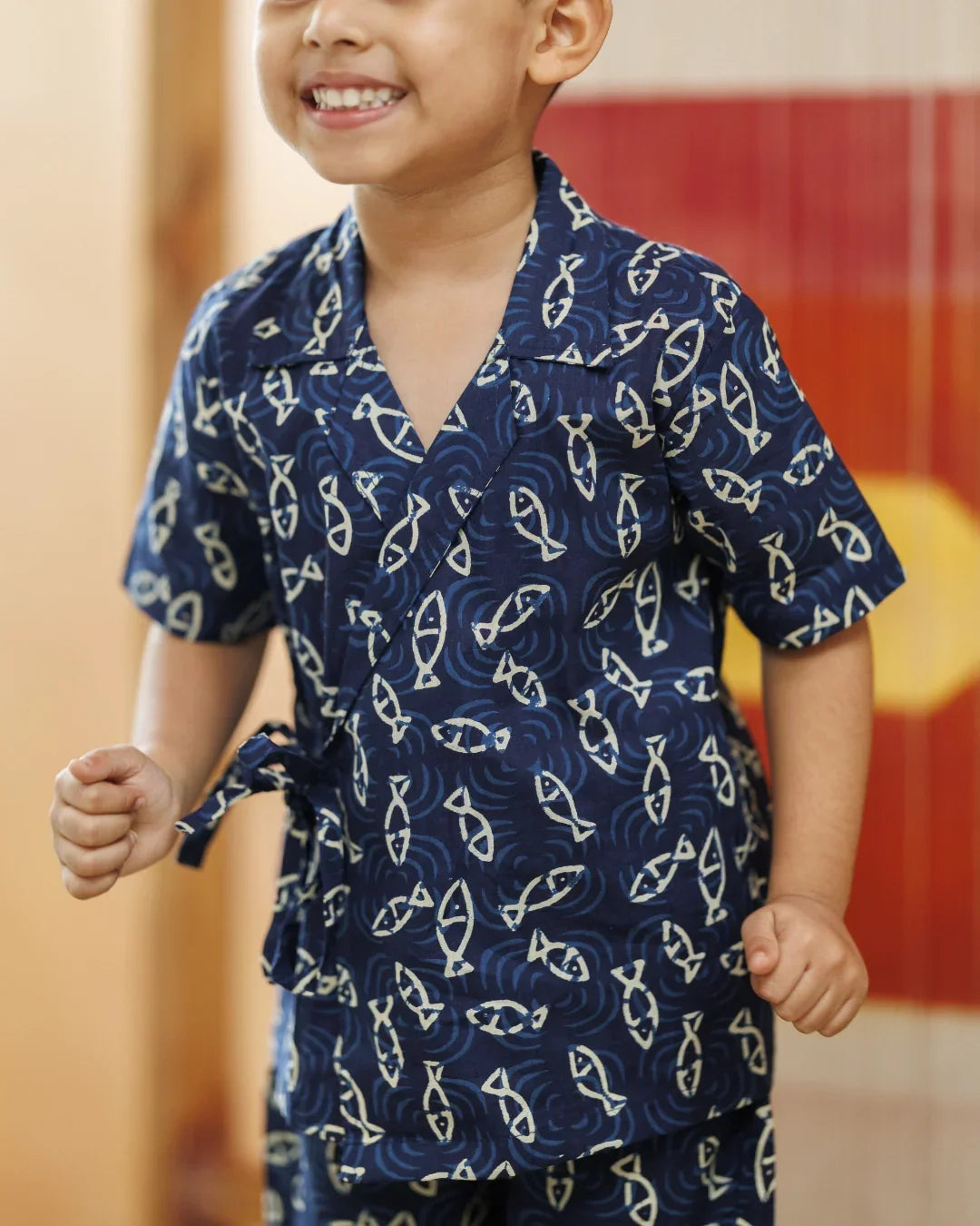 Smiling child in navy blue organic cotton shirt with white fish pattern, playful kidswear