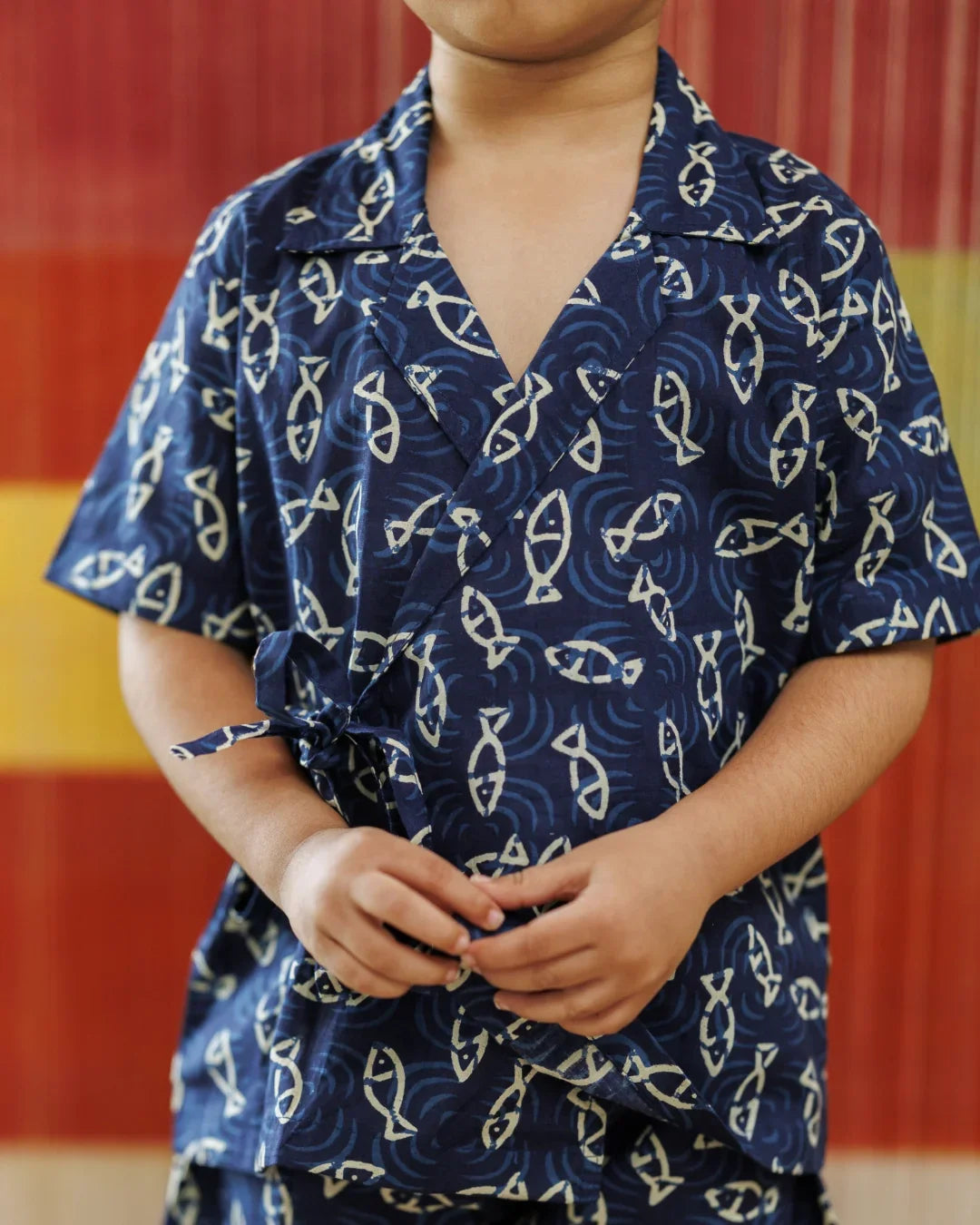 Child wearing blue organic cotton shirt with white fish pattern, short sleeves, summer kidswear