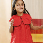 Smiling young girl in a bright red organic cotton top with scalloped collar, indoors