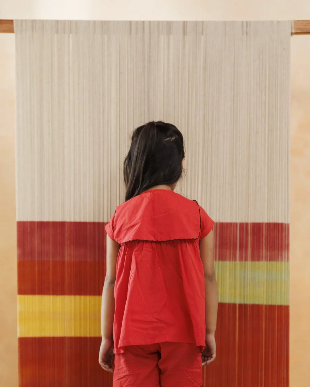 Young child in red organic cotton outfit standing in front of a colorful textile backdrop